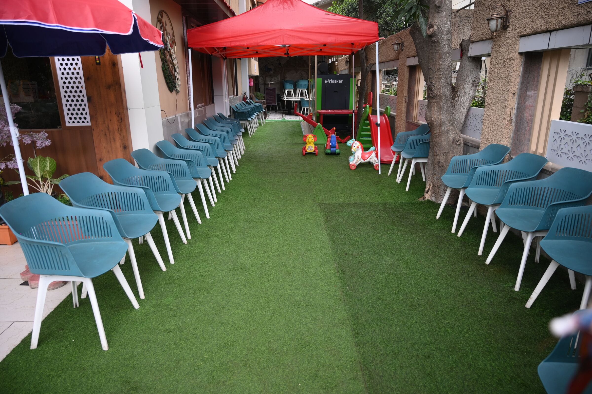 The garden lawn: rows of blue shell chairs, red umbrellas and a children's play corner