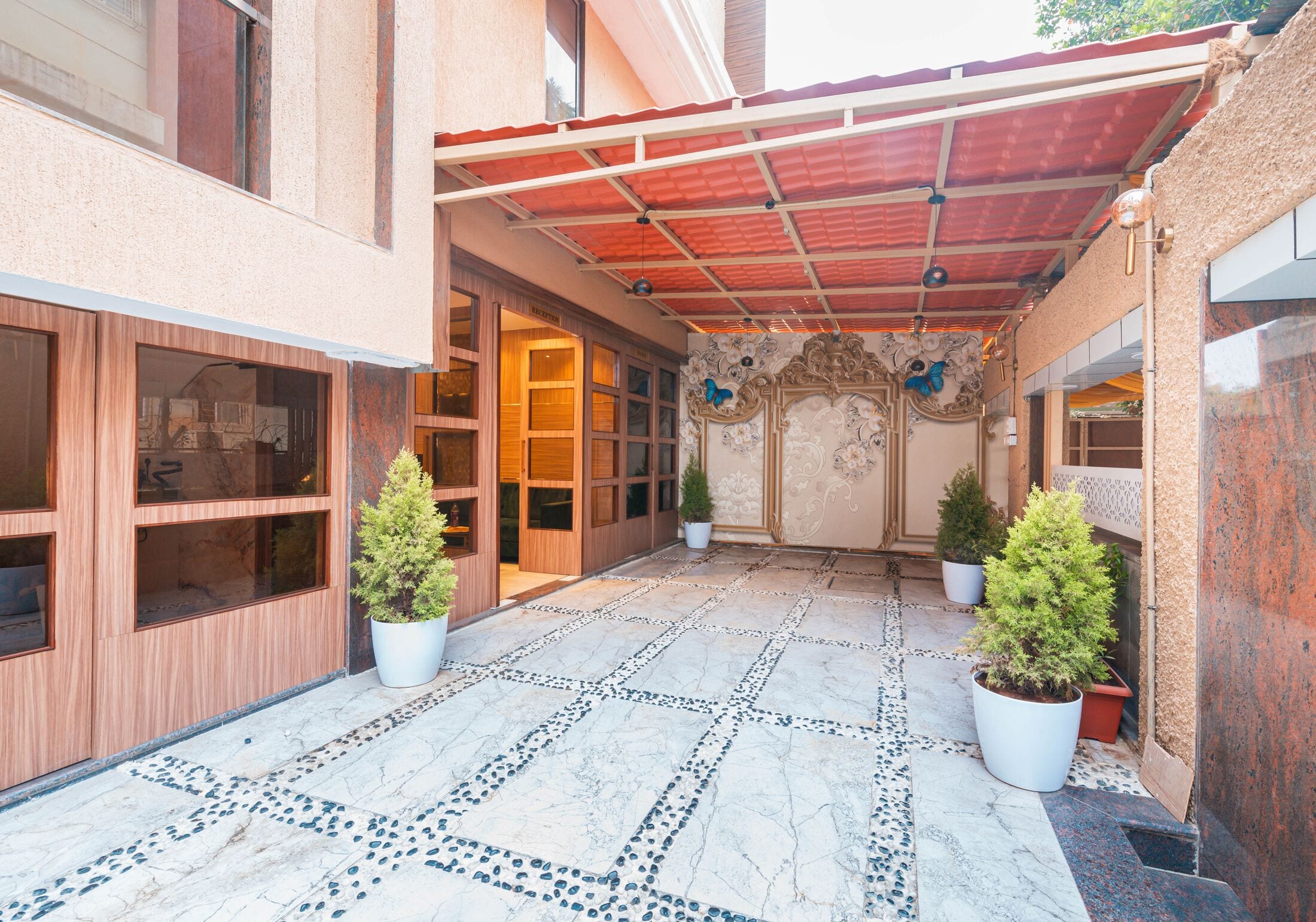 The entrance courtyard: pebble-inlaid stone paving under a red canopy, with potted conifers