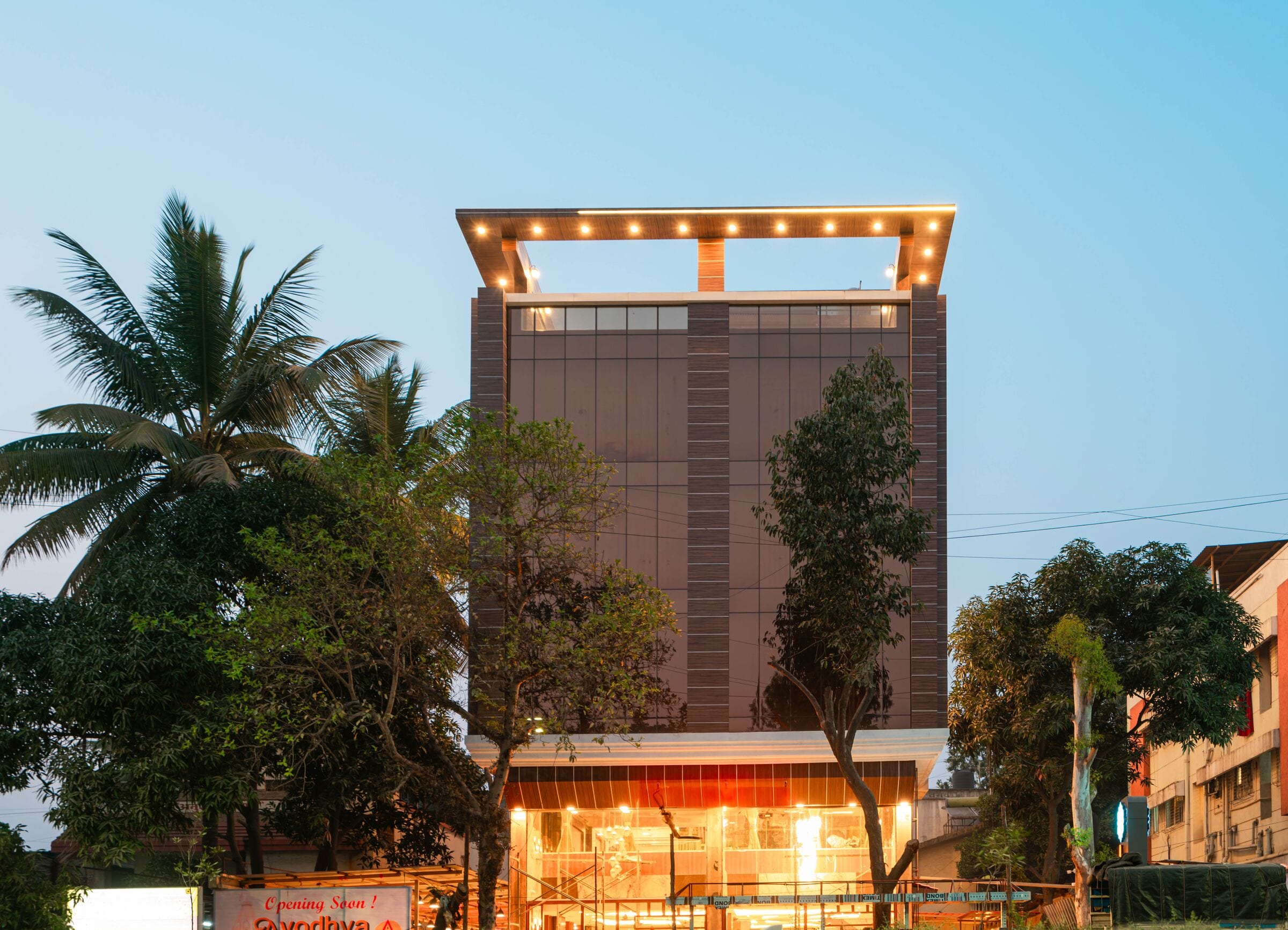 Lemonwood Suites at dusk: the square rooftop frame outlined in warm bulbs above the glowing ground-floor restaurant